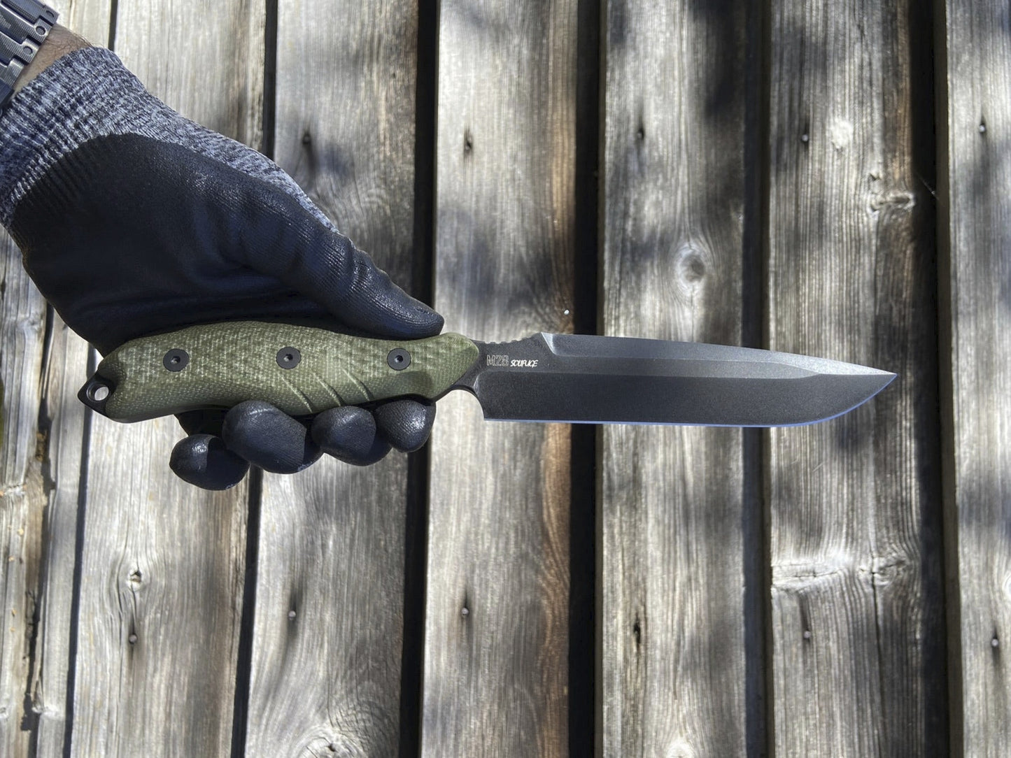 Hand holding a knife with a green handle against a wooden background