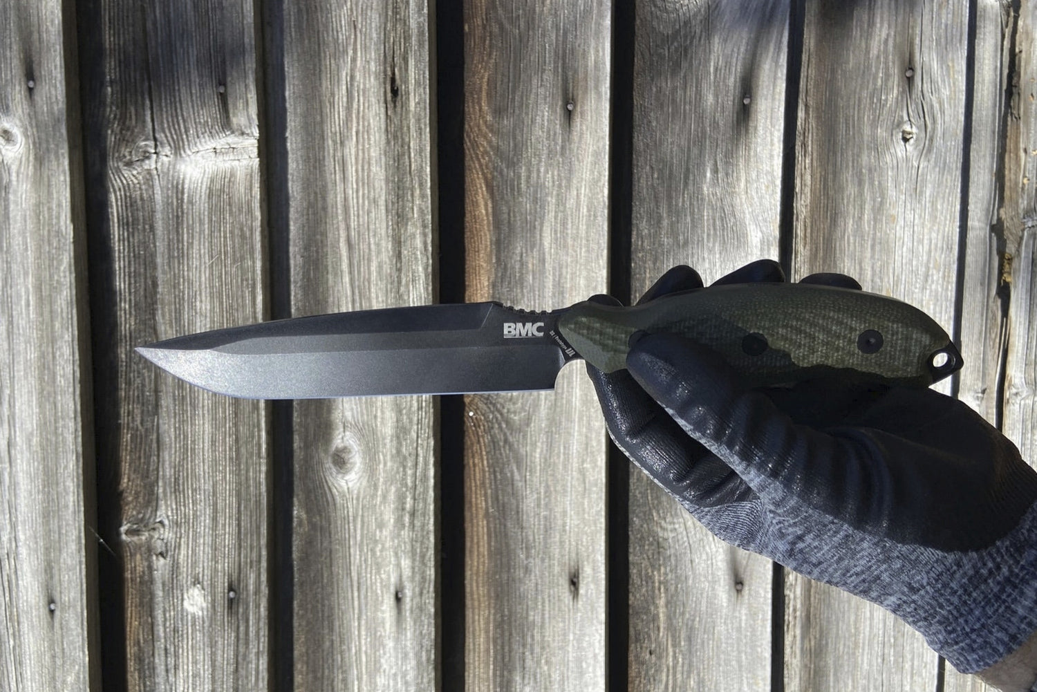 Hand holding a knife with a visible brand logo against a wooden background
