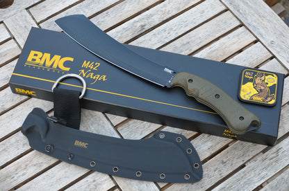 BMC M42 Naga parang with an olive green handle, shown with its black branded box, black sheath, and a small patch on a weathered wooden slat surface.