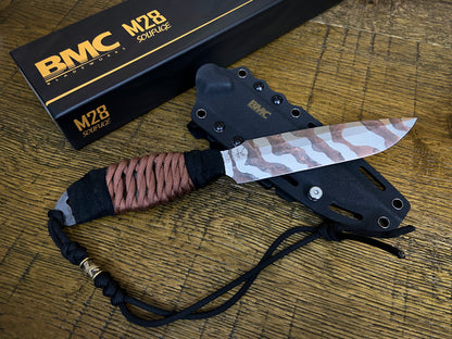 BMC M28 Solifuge fixed blade knife with a tiger-stripe pattern blade, wrapped handle, and black sheath, displayed on a wooden surface next to its black branded box.