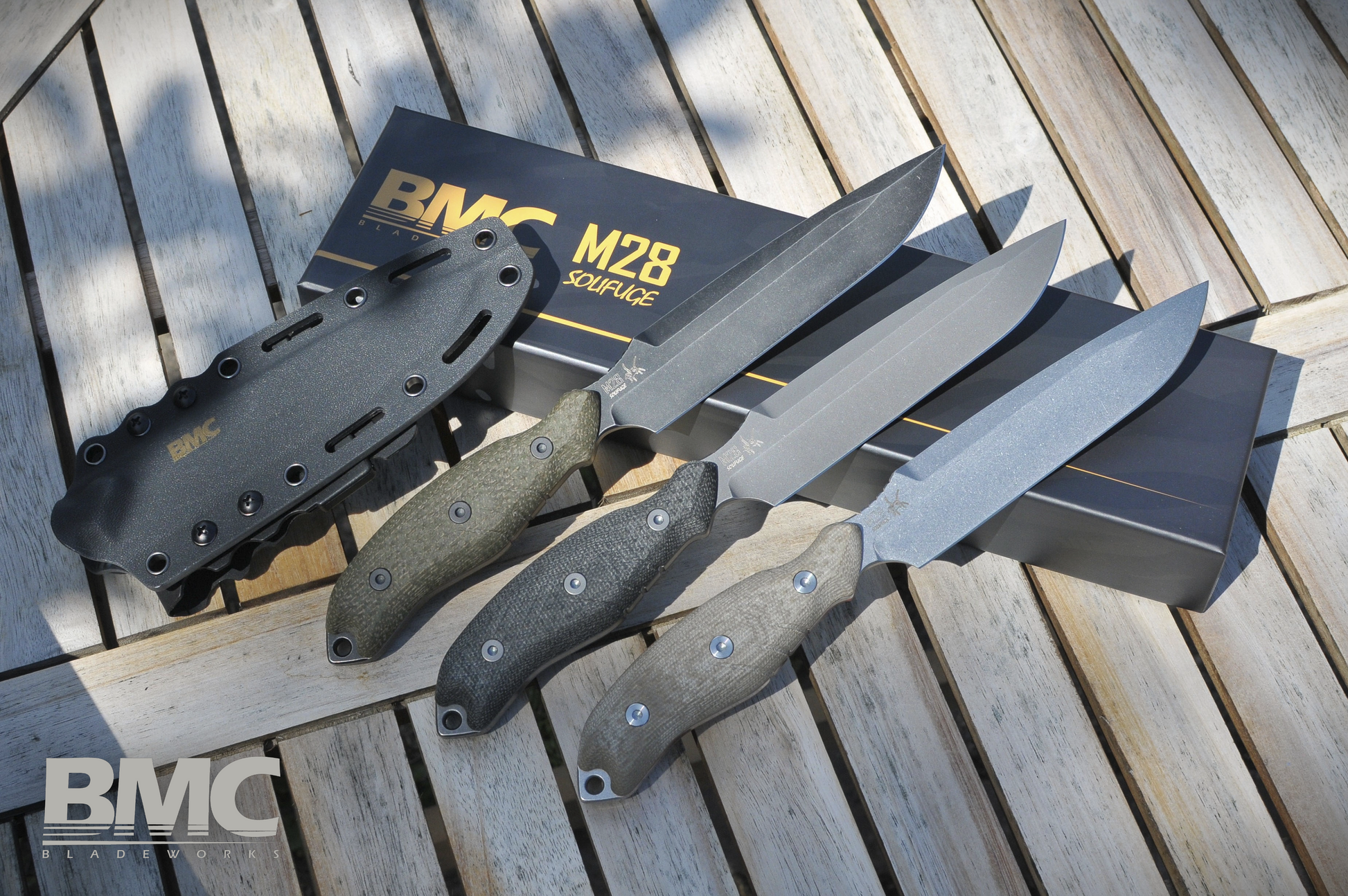 Set of BMC M28 knives with sheath on a wooden surface, featuring BMC branding.