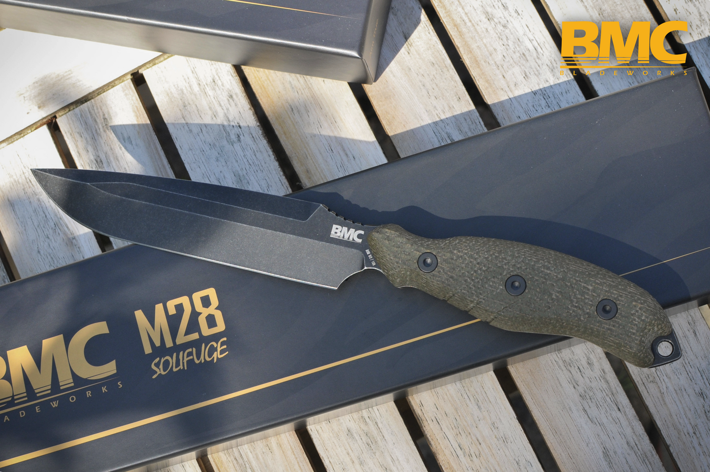 BMC M28 Knife with sheath on a wooden surface, featuring BMC branding.